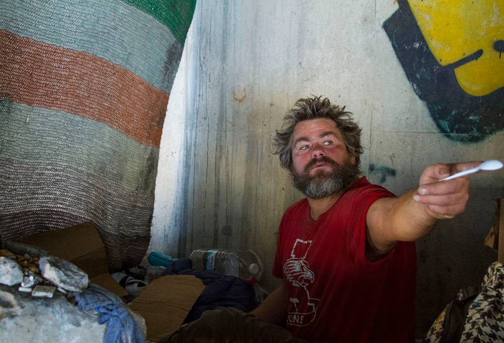 Homeless man in red t-shirt eats in his tent